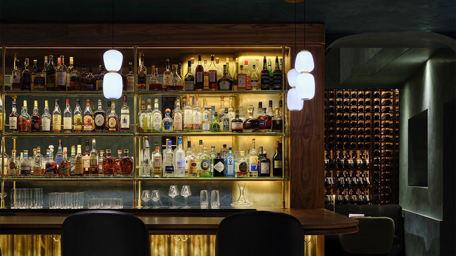 The brighly lit, golden-hued bar at Providence with a display wine cellar visible in another room